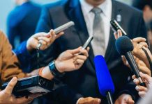 Man in suit surrounded by microphones at press conference