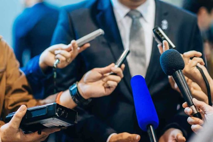 shutterstock_471987565-1 Man in suit surrounded by microphones at press conference