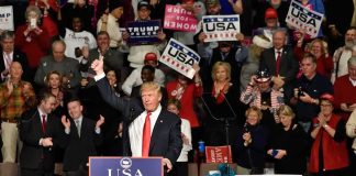 Donald Trump addresses a rally crowd at a podium, raising his fist