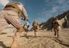 Soldiers in desert camouflage running across rocky terrain