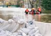 Sandbags stacked near a flooded street with rescue workers in a boat
