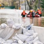 Sandbags stacked near a flooded street with rescue workers in a boat