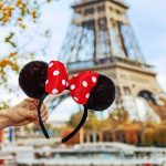 hand holding polka dot bow mouse ears in front of the Eiffel Tower