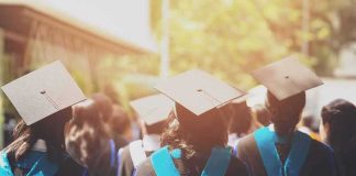 Graduates in caps and gowns walking at an outdoor ceremony