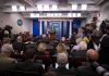 Press secretary at podium addressing reporters in briefing room