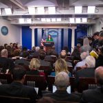 Press secretary at podium addressing reporters in briefing room