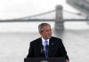 George W. Bush speaking at a podium with a bridge over water in the background