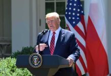 Donald Trump speaking at a podium with U.S. and Polish flags behind him