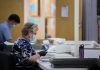 Election workers wearing masks process mail-in ballots at tables