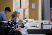 Election workers wearing masks process mail-in ballots at tables