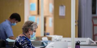 Election workers wearing masks process mail-in ballots at tables