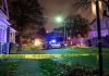Police car blocks residential street at night behind caution tape