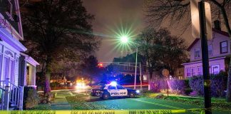 Suspect Charged After Gunfire at High School Football Game Police car blocks residential street at night behind caution tape