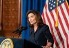 Kathy Hochul speaking at a podium with microphones and a U.S. flag behind her