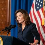 Kathy Hochul speaking at a podium with microphones and a U.S. flag behind her