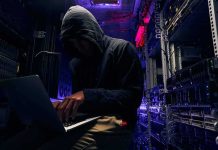 Hooded person using a laptop in a dark server room