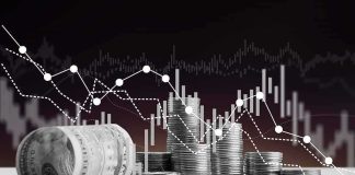 Stacks of coins and rolled dollar bills with falling financial charts