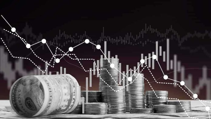 Stacks of coins and rolled dollar bills with falling financial charts