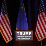 Trump Links Ukraine War to Fuel Costs Podium with campaign sign between American flags