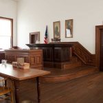 Victim Stunned: Judge Dismisses Toxic Poisoning Case Interior of a historic courtroom with wooden furniture and an American flag