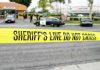 yellow sheriff's line tape blocks a street near police cars
