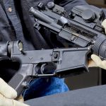 Person assembling a rifle with gloved hands