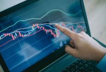 Hand pointing at stock market graph on laptop screen