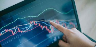 Hand pointing at stock market graph on laptop screen