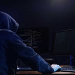 Hooded figure using dual monitors in dark room