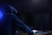 Hooded figure using dual monitors in dark room