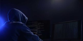Hooded figure using dual monitors in dark room