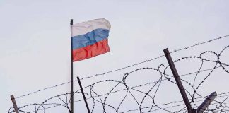 Barbed wire fence with Russian flag in background