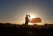 Silhouette holding USA flag against sunset sky