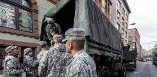 Soldiers gather around a military truck on street