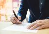 Person signing a document with a pen