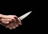 Hand holding a knife against a black background