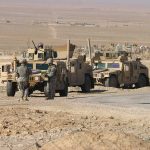 Soldiers standing near armored vehicles in desert terrain