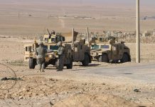Soldiers standing near armored vehicles in desert terrain
