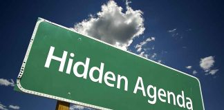 Green road sign reading Hidden Agenda sky background
