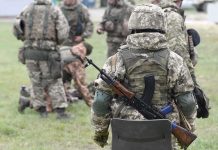 Soldiers in camouflage gear gathered on grass field