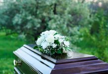 Coffin with white flowers outdoors in green surroundings