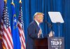 Person speaking at podium with flags in background