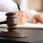 Judge gavel on desk with person writing