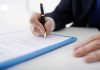 Person signing a document with a pen
