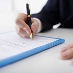 Person signing a document with a pen