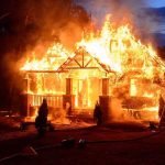House engulfed in flames with firefighters present