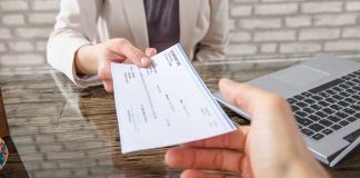 Hands exchanging a check near a laptop