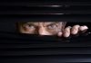 Man peeking through half-open black blinds.