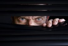 Man peeking through half-open black blinds.