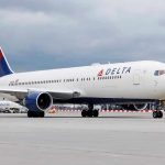 Delta Airlines airplane on airport runway, cloudy sky